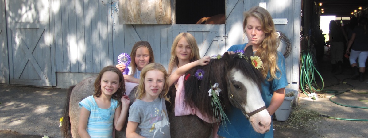 Kids with a pony wearing flowers and a ribbon